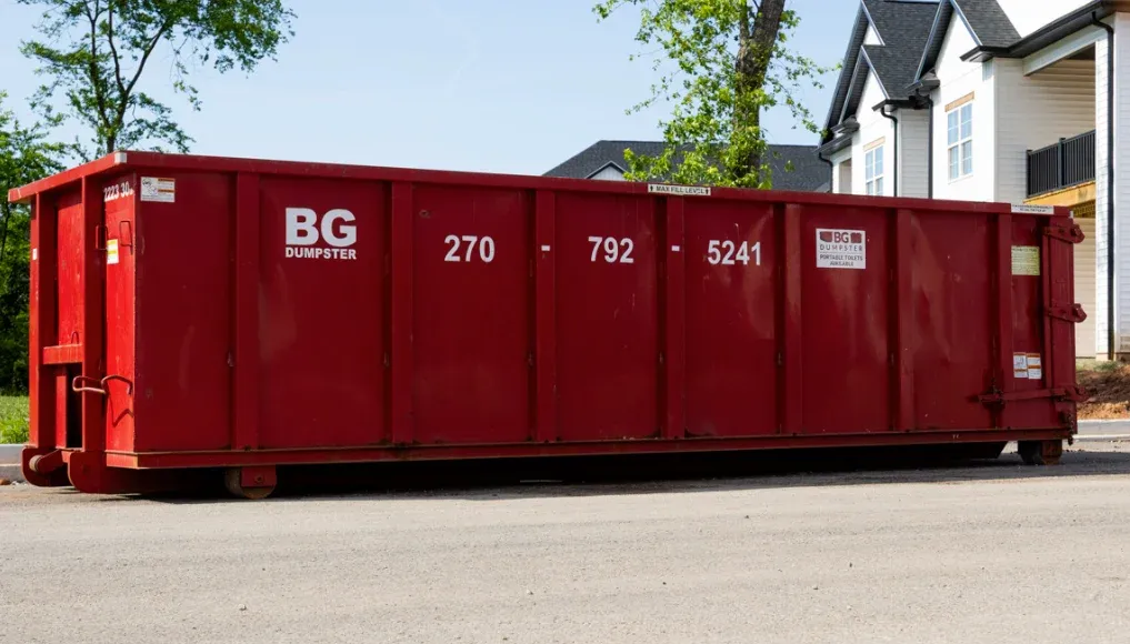 A red BG Dumpster roll-off container at a commercial property