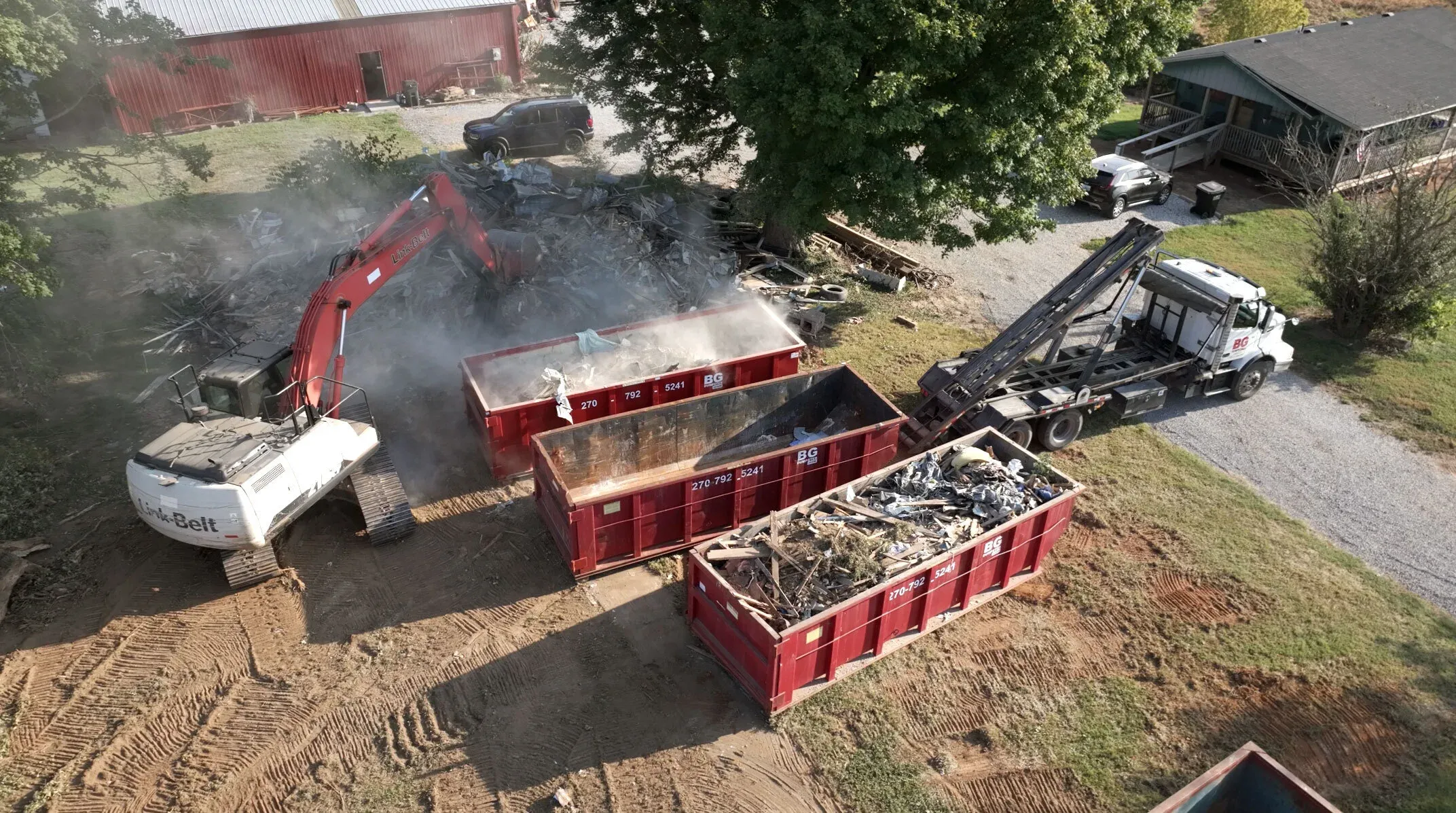 An excavator loading demolition debris into BG Dumpster roll-off containers