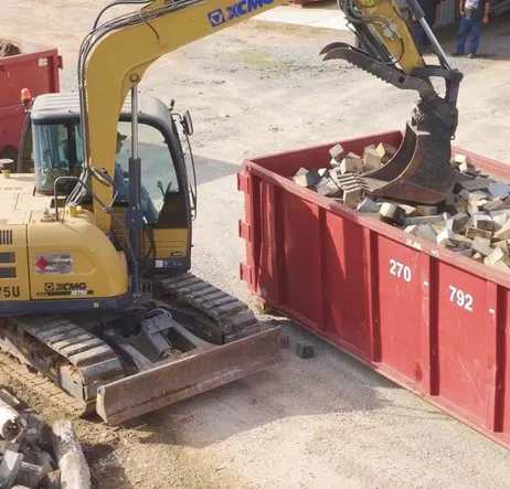 An excavator loading construction debris into a BG Dumpster container