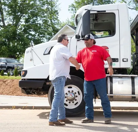 A homeowner greeting a BG Dumpster team member beside a delivery truck