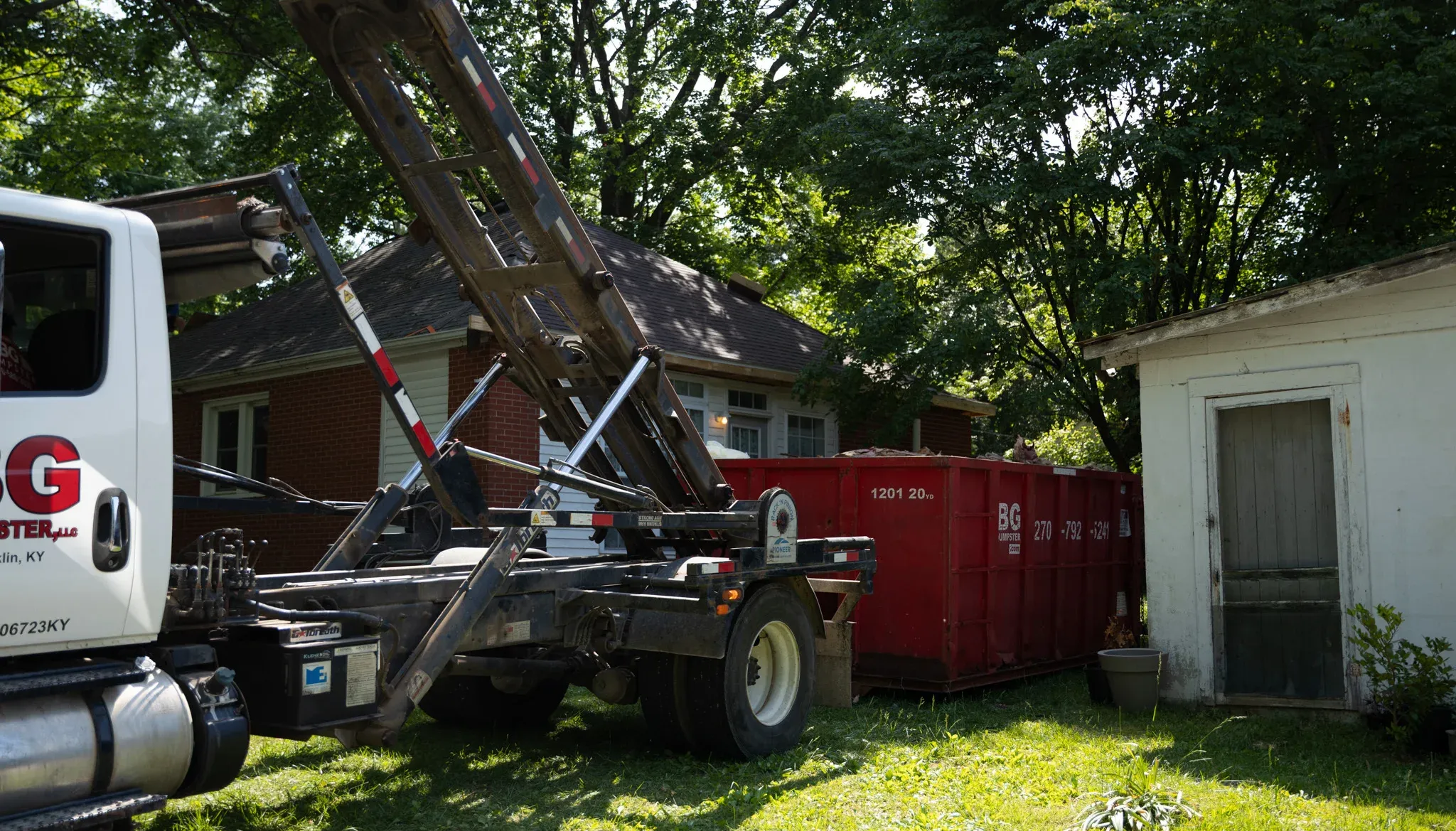 A BG Dumpster truck delivering a roll-off container beside a home