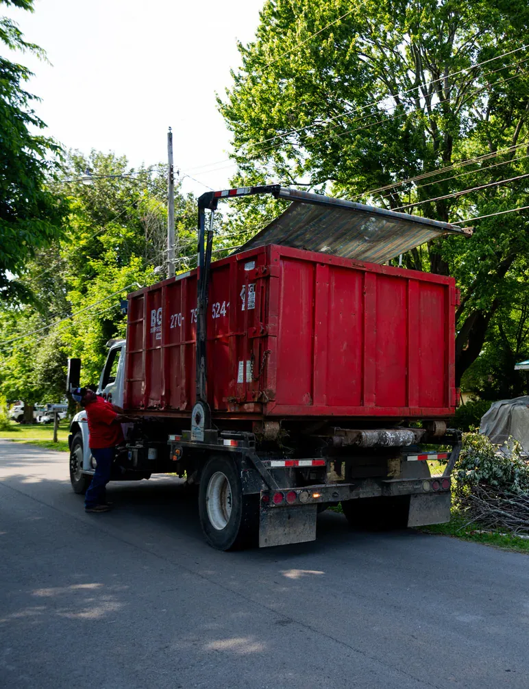A BG Dumpster driver with a roll-off truck on a tree-lined residential street