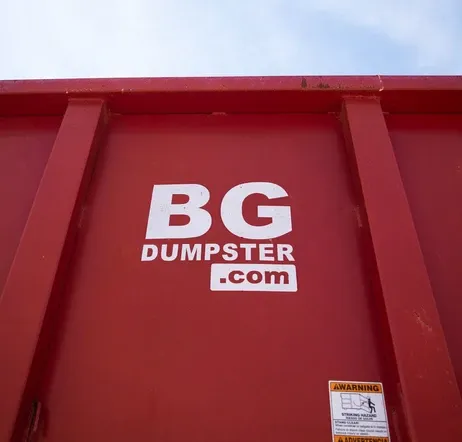 A red BG Dumpster container ready for roofing debris